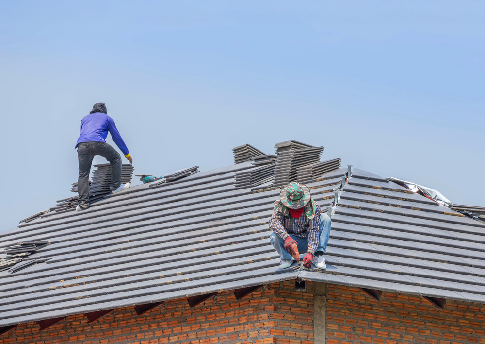 Roofer installing concrete tiles on the roof house in residential construction site
